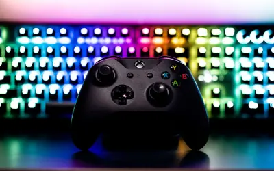 Czarny kontroler Xbox na tle podświetlanej klawiatury RGB. Idealny sprzęt do **grania na długie godziny**.