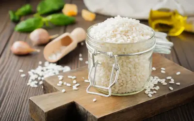 Słoik pełen ryżu **arborio**, idealnego do kremowego risotto. Obok czosnek, bazylia i oliwa.