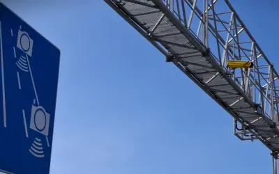 Niebieski znak informuje o odcinkowym pomiarze prędkości S7. Żółta kamera zamontowana na konstrukcji nad drogą rejestruje pojazdy.