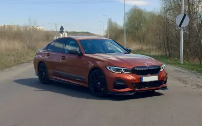Pomarańczowe BMW 330i G20 na drodze, z widocznymi czarnymi felgami i detalami aerodynamicznymi.