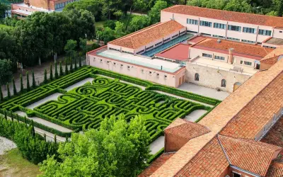Un giardino con un intricato labirinto borges, circondato da edifici con tetti rossi e alberi verdi.