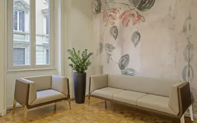 Eleganckie fotele i sofa na tle tapety z motywem kwiatowym. Czy można kleić tapetę na tapetę? Tutaj wygląda to stylowo.