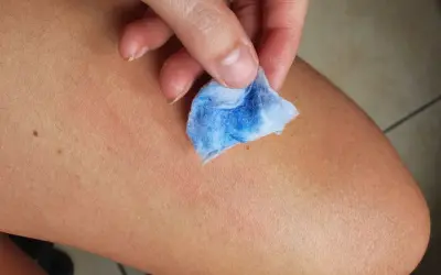 Mano che pulisce la pelle con un dischetto di cotone blu, mostrando come togliere la vernice dalla pelle in modo efficace.