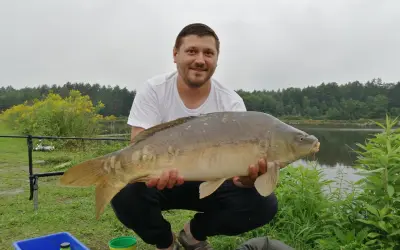 Szczęśliwy wędkarz z okazałym karpiem złowionym na łowiskach karpiowych podkarpackich.