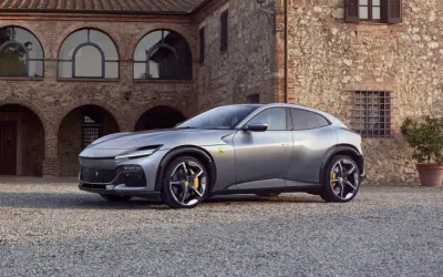 Srebrny Ferrari SUV Purosangue zaparkowany przed kamiennym budynkiem z łukowymi oknami.