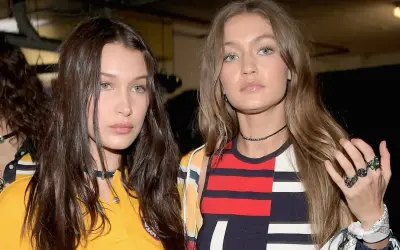 Bella Hadid i Gigi Hadid, siostry i modelki, w modnych stylizacjach. Bella ma ciemne włosy, Gigi jasne. Ich wiek jest nieistotny wobec ich talentu.