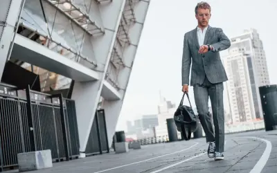 Elegancki garnitur i trampki na wesele – młody mężczyzna sprawdza zegarek, idąc z torbą obok nowoczesnego budynku.