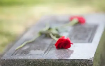 Dwie czerwone róże na kamiennej płycie nagrobnej symbolizują pożegnanie pogrzebowe i wieczną pamięć.