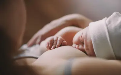 Czułe chwile karmienia piersią. Dziecko ulewa mimo odbicia, ale mama czule je przytula.