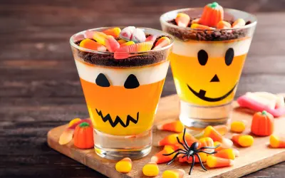 Deliciosa gelatina Halloween para niños, con capas de naranja y blanco, decorada como calabaza y cubierta de dulces.