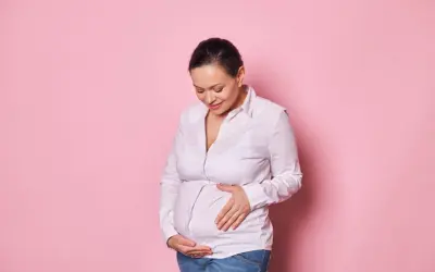 Kobieta w ciąży w wieku 45 lat z uśmiechem na twarzy delikatnie dotyka swojego brzucha.