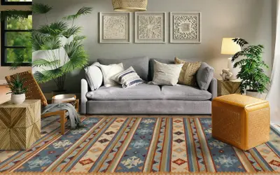 Tappeto 2 metri per 3 con motivi geometrici in blu, beige e arancione, che copre il pavimento di un soggiorno moderno con divano grigio e piante verdi.