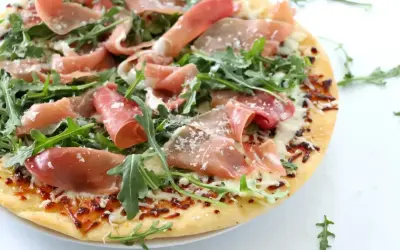 Pyszna pizza prosciutto z rukolą i parmezanem, idealna na letni wieczór.