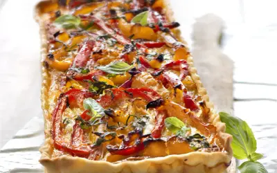 Tarte rectangulaire aux poivrons rouges et jaunes grillés, garnie de basilic frais. Un délice coloré et savoureux.
