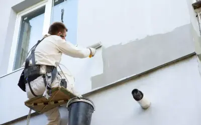 Pracownik na wysokościach maluje elewację budynku, używając wałka.