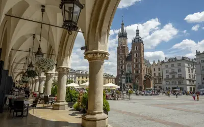 Kraków Rynek tętni życiem pod arkadami Sukiennic. W tle Bazylika Mariacka i tłumy spacerowiczów.