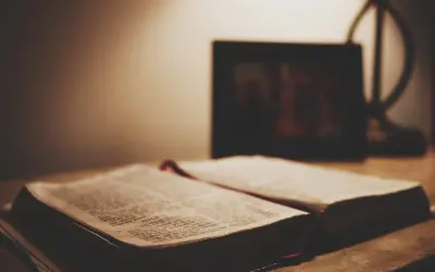 Otwarta Biblia na stole, obok ramka ze zdjęciem. Czy granie w lotto to grzech? Szukamy odpowiedzi w Piśmie Świętym.