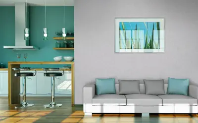 Modernes Wohnzimmer mit Vliestapete tapezieren. Ein weißes Sofa mit blauen und grauen Kissen steht vor einer Wand mit einem Bild von Gräsern. Daneben eine Küche mit Bar.