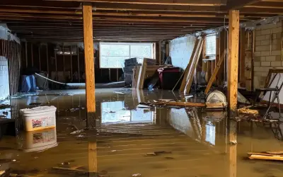 Un **garage inondé** avec de l'eau boueuse recouvrant le sol, des débris flottants et des matériaux de construction endommagés.