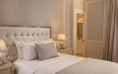 Elegancka sypialnia z dużym łóżkiem, pikowanym zagłówkiem i stylowymi lampkami nocnymi. Widok na łazienkę i zasłony. Idealne miejsce dla wynajmującego szukającego komfortu.