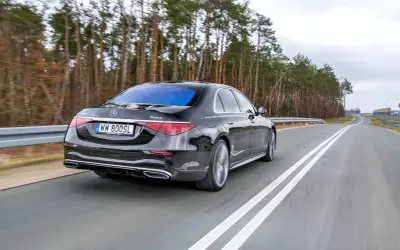 Czarny Mercedes S400d 4Matic sunie po drodze wśród drzew.