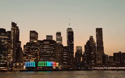 Wieczorny widok na Manhattan podczas zwiedzania Nowego Jorku. Podświetlone wieżowce odbijają się w wodzie.