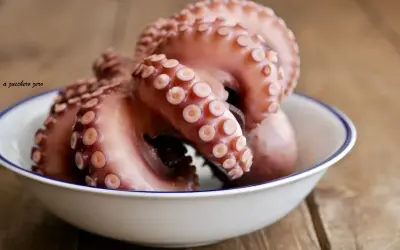 Pulpo listo para cocer en un cuenco blanco con borde azul, sobre una mesa de madera rústica.