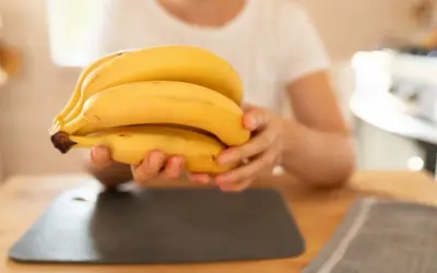Dłoń trzymająca kiść żółtych bananów na drewnianym stole.