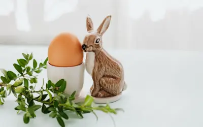 Wielkanocne jajka w kieliszku, obok ceramiczny zajączek i gałązka bukszpanu.