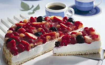 Eine einfache Torte mit frischen Beeren, bedeckt mit Tortenguss. Daneben zwei Tassen Kaffee.