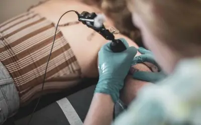 Tatuador con guantes azules haciendo un tatuaje de puñal en la pierna de una persona.