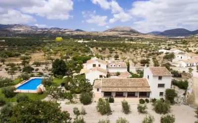 El cortijo el serbal, rodeado de olivos y montañas, con piscina azul y casas blancas de tejados terracota.