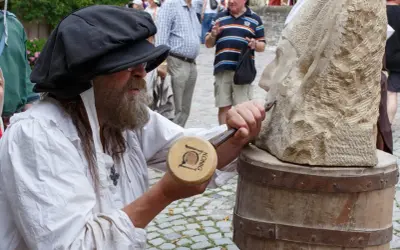 Steinmetz bei der Arbeit am Bad Wimpfen Zunftmarkt. Ein Mann mit Bart und schwarzer Kappe meißelt an einer Steinskulptur.