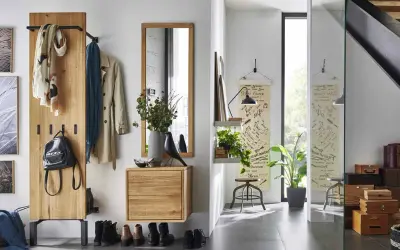 Une entrée dans un salon moderne avec un portant en bois, des manteaux, un sac à dos, des tableaux et une étagère avec des plantes.