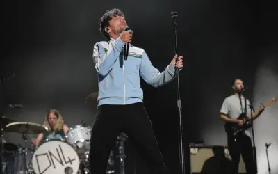 Louis Tomlinson na scenie, śpiewający do mikrofonu. W tle perkusista i gitarzysta.