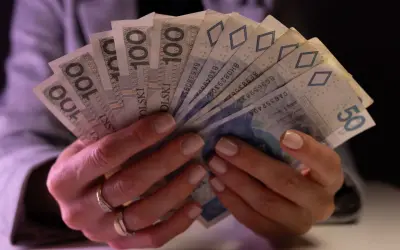 Dłonie trzymające plik banknotów 100 zł i 50 zł. Taki jest koszt życia.
