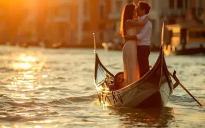 Un couple s'embrasse tendrement dans une gondole, baigné par la lumière dorée du coucher de soleil. Venise, ville des amoureux, offre un cadre idyllique pour cet instant magique.