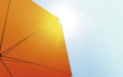 Ein orangefarbener Sonnenschirm schützt vor der Sonne. Seine Struktur ist sichtbar, während Sonnenstrahlen durchscheinen. Diethylhexyl Butamido Triazone schützt die Haut.