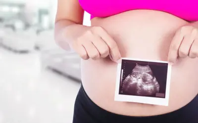 Ciężarna kobieta trzyma zdjęcie USG płodu na tle rozmazanego wnętrza.