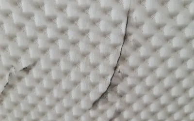 Biała tkanina z pikowanym wzorem i ciemnymi smugami.