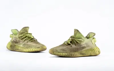Para zielonych adidas Yeezy 350 z charakterystyczną, prążkowaną podeszwą, gotowe na miejskie przygody.