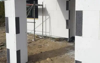 Budowa domu z bloczków styropianowych. Zastanawiasz się, czym przykleić styropian do blachy? Tutaj widzisz fragmenty ścian i słupa z białego styropianu z czarnymi wstawkami.
