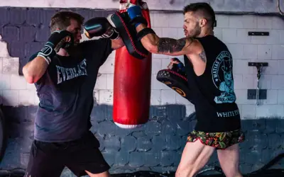 Two boxers train in a gym. One throws a punch while the other uses pads to parry boxing.