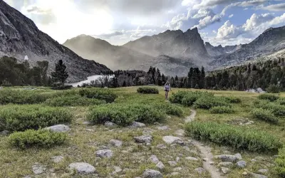 Wanderer auf dem Continental Divide Trail wandern durch eine bergige Landschaft mit einem See und bewaldeten Hängen.