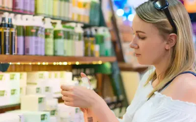 Kobieta testuje kosmetyk, który zawiera benzyl alcohol, na dłoni. W tle widać półki pełne produktów.