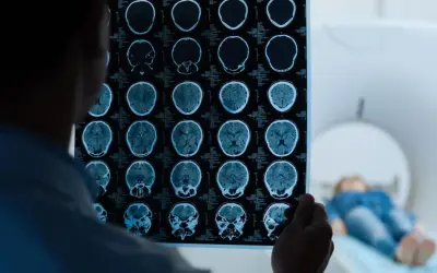 Lekarz analizuje wyniki rezonansu magnetycznego głowy, wykonanego w ramach testu na wstrząs mózgu. W tle pacjent leży w aparacie MRI.