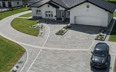 Nowoczesny dom z podjazdem z kamienia, który prowadzi do garażu. Czarny samochód zaparkowany na podjeździe.