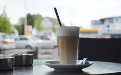 En hög latte macchiato med skummig mjölk och en sked, redo att avnjutas vid ett cafébord utomhus.