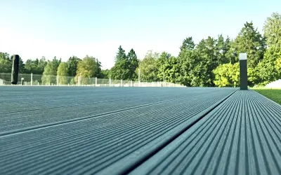 Szara deska kompozytowa tworzy nowoczesną nawierzchnię tarasu, otoczoną zielenią i jasnym niebem.