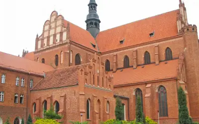 Majestatyczna pelplińska katedra z cegły, z charakterystycznymi dachami i wieżą, góruje nad otoczeniem.